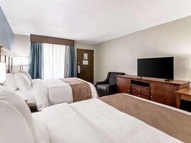 A hotel room with two beds, a desk, a television, and a chair.