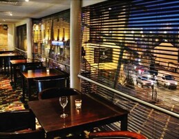 Un restaurante con mesas y sillas, un suelo estampado y vista a la calle a través de una ventana con diseño.