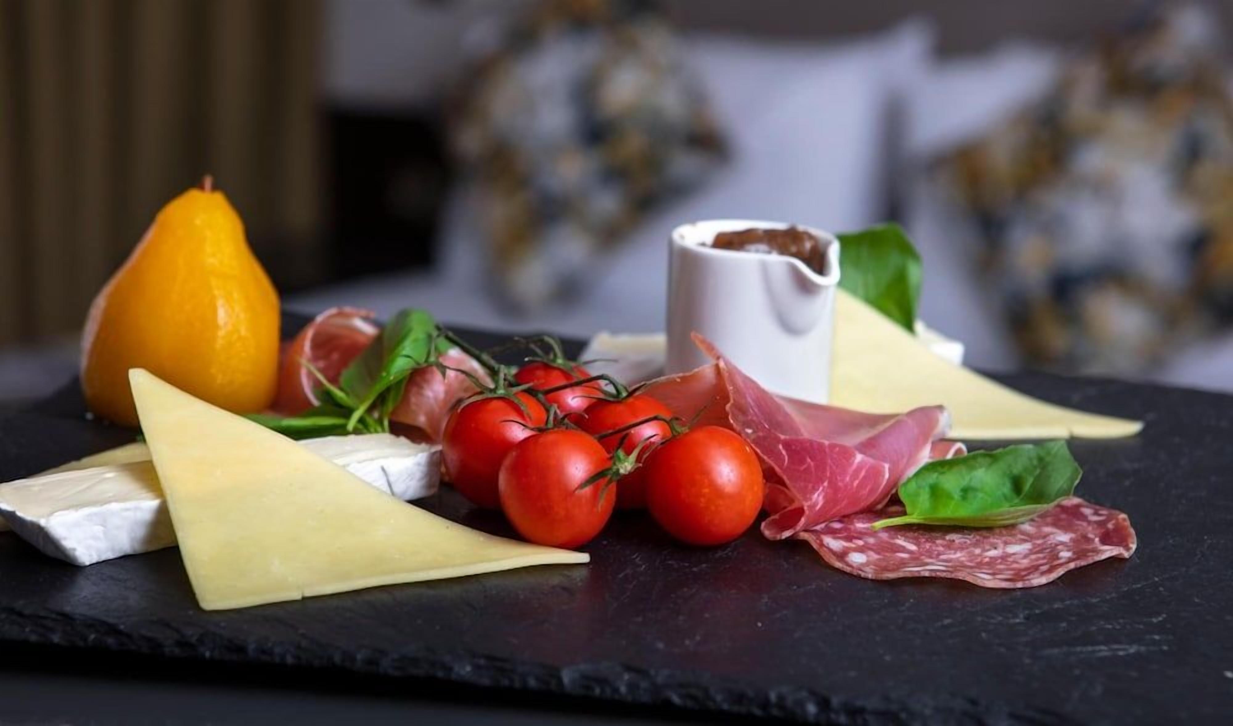 Une sélection de fromages, de charcuteries et de tomates fraîches, présentée sur une planche en ardoise.