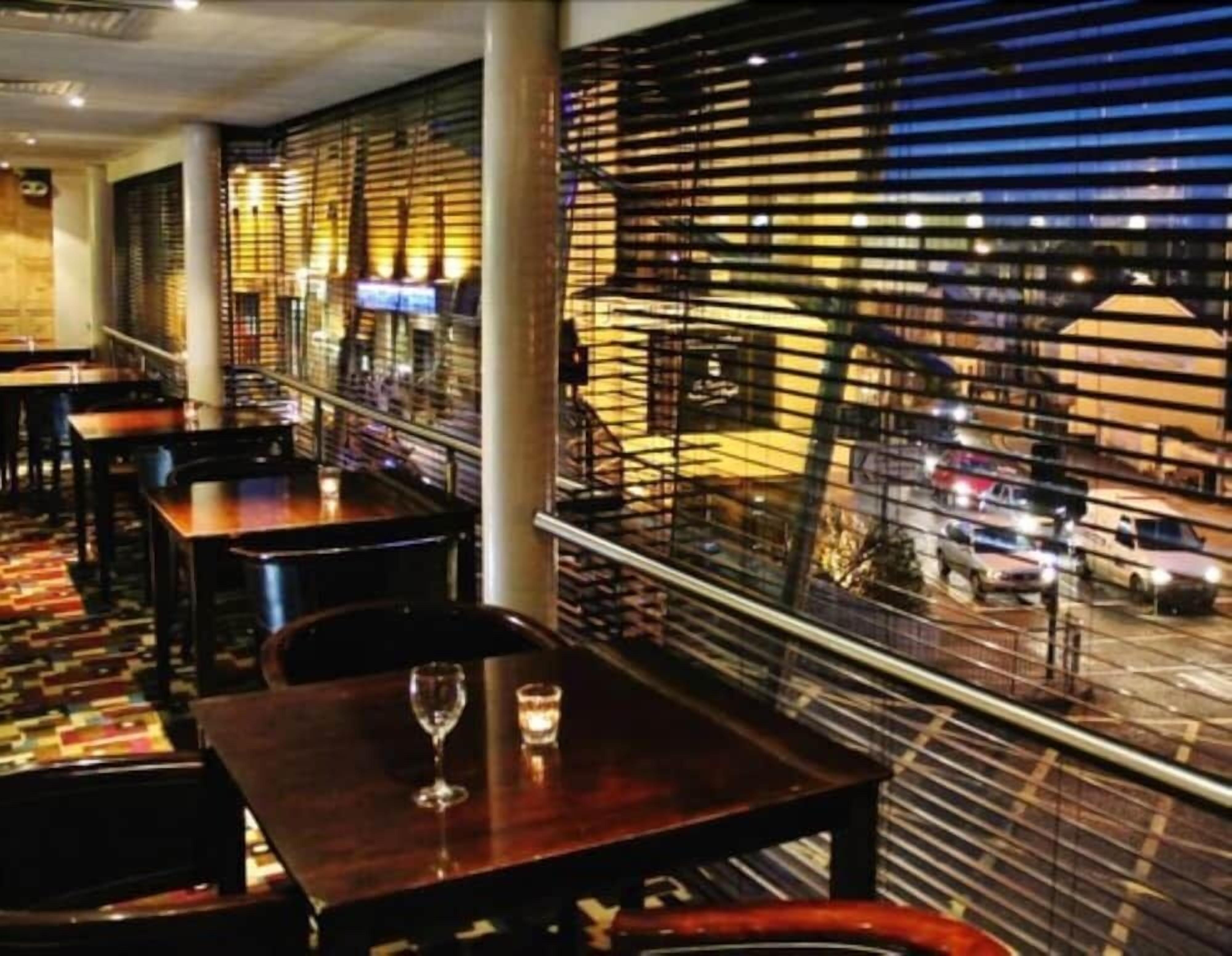 A restaurant with tables and chairs, a patterned floor, and a view of the street outside through a patterned window.