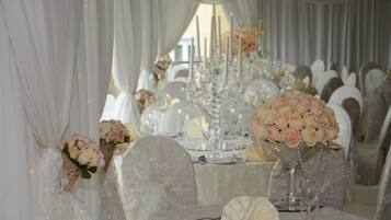 A wedding reception table with white tablecloths, floral centerpieces, and candle holders.