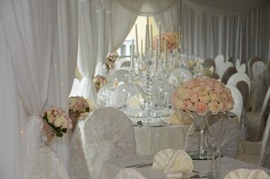 A wedding reception table with white tablecloths, floral centerpieces, and candle holders.