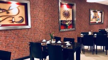 Un comedor con paredes de ladrillo, obras de arte enmarcadas y mesas y sillas de comedor negras.