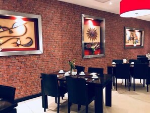 A dining area with brick walls, framed artwork, and black dining tables and chairs.