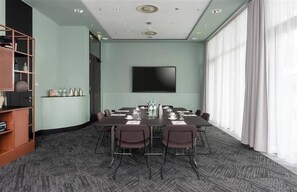Un salón de conferencias con una gran mesa, sillas, un televisor de pantalla plana y una estantería.