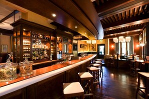 Zona de bar con una barra curva, taburetes y una variedad de botellas y vasos.