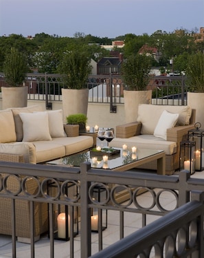 An outdoor seating area with wicker furniture, a glass table, and candles. - Kimpton Lorien Hotel and Spa (Alexandria)