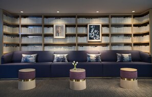 A modern living room with a dark blue sofa, three round side tables, and a bookshelf filled with books. - Kimpton Lorien Hotel and Spa (Alexandria)
