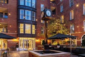 Un patio de hotel con un reloj, asientos al aire libre y la entrada del edificio.