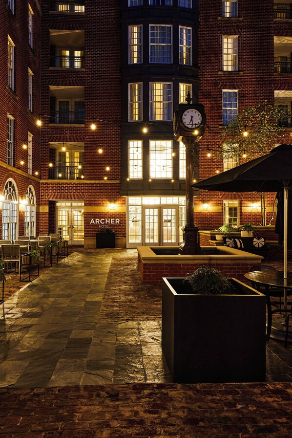 Patio de hotel con un reloj, asientos al aire libre y un letrero del Archer Hotel.