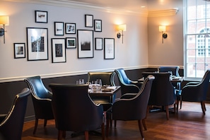 A restaurant with black leather chairs, framed artwork on the wall, and a window providing natural light. - Kimpton Lorien Hotel and Spa (Alexandria)
