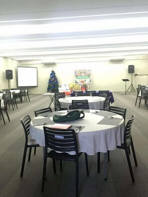 A conference room with round tables, chairs, a projector screen, a Christmas tree, and a banner. - Blue Lagoon Inn Suites (Puerto Princesa)
