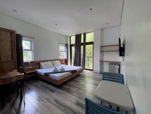 A room with a bed, a desk, a chair, a TV, and large windows. - Blue Lagoon Inn Suites (Puerto Princesa)