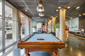 A pool table in a modern indoor setting with large windows and indoor plants. - Select Hotel Apple Park Maastricht (Maastricht)