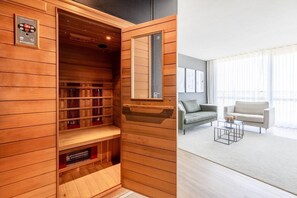 Un sauna avec des panneaux en bois, un panneau de commande et un miroir. À côté se trouve un salon avec un canapé, une table basse et une fenêtre avec des rideaux.