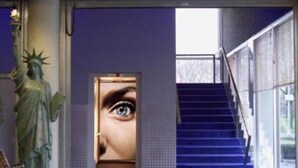 Un hall d’entrée avec une statue, un grand écran numérique, un escalier et un banc.