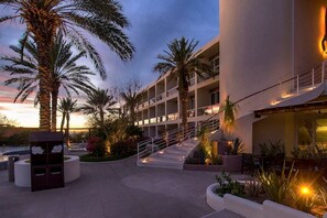 Een hotel met een modern ontwerp, met een centrale trap, meerdere balkons en palmbomen.