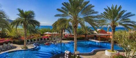 A resort pool with palm trees, lounge chairs, and a clear view of the ocean.