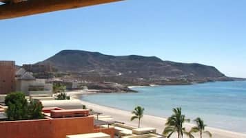 Um hotel à beira-mar com vista para a praia, uma montanha ao fundo e céu claro.