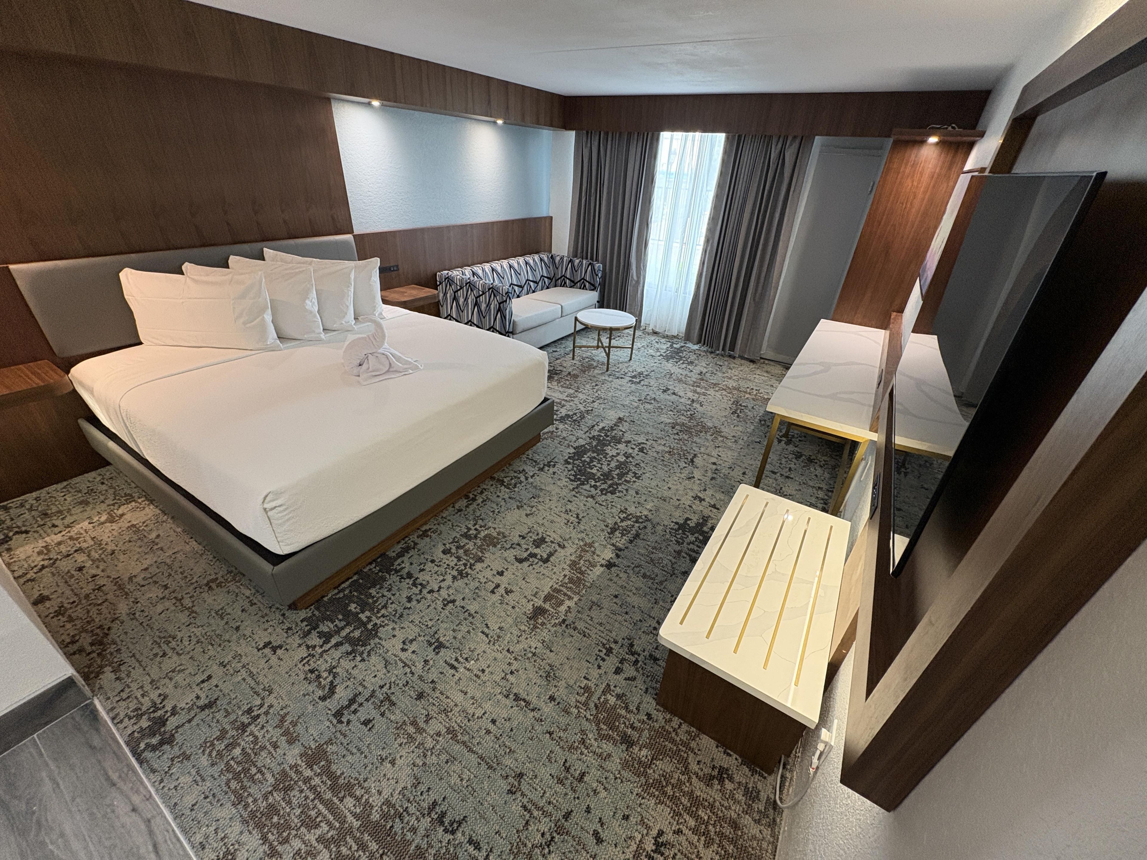 Une chambre d’hôtel avec un grand lit, un canapé, une petite table, un miroir et un téléviseur.