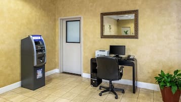 A room with a self-service ATM, a desk with a computer, a chair, and a potted plant.