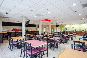 Une cafétéria avec de nombreuses tables et chaises, un coin bar et un comptoir où sont exposés les plats proposés.