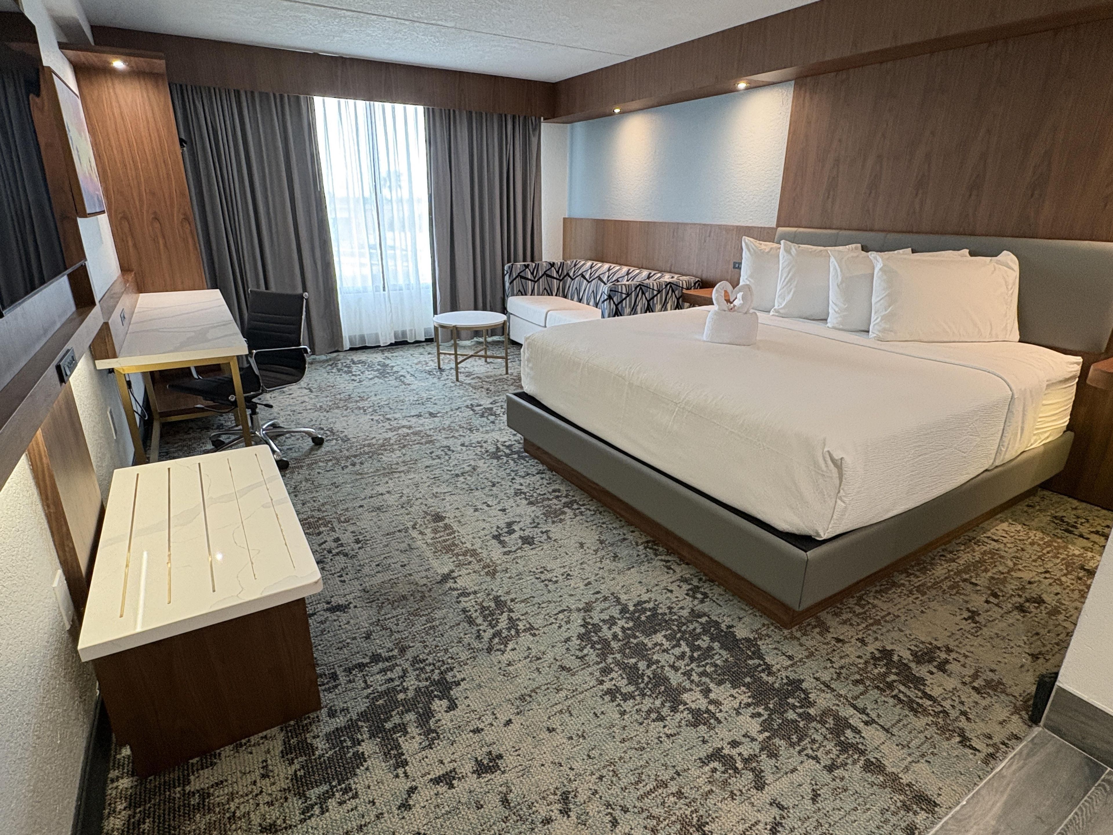 Une chambre d’hôtel avec un grand lit, un bureau, une chaise et une petite table.