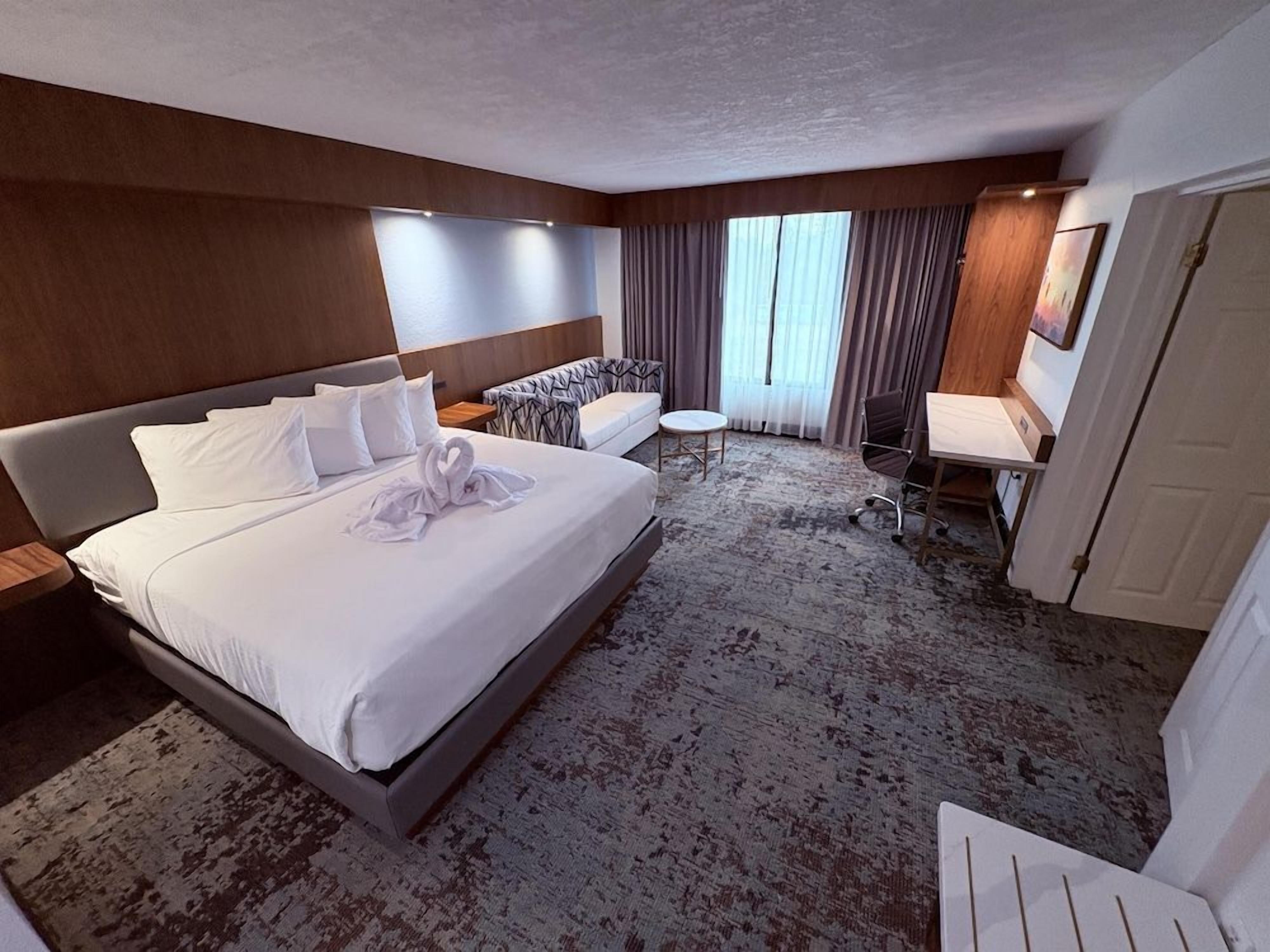 A hotel room with a large bed, a seating area with a table and chairs, and a door.