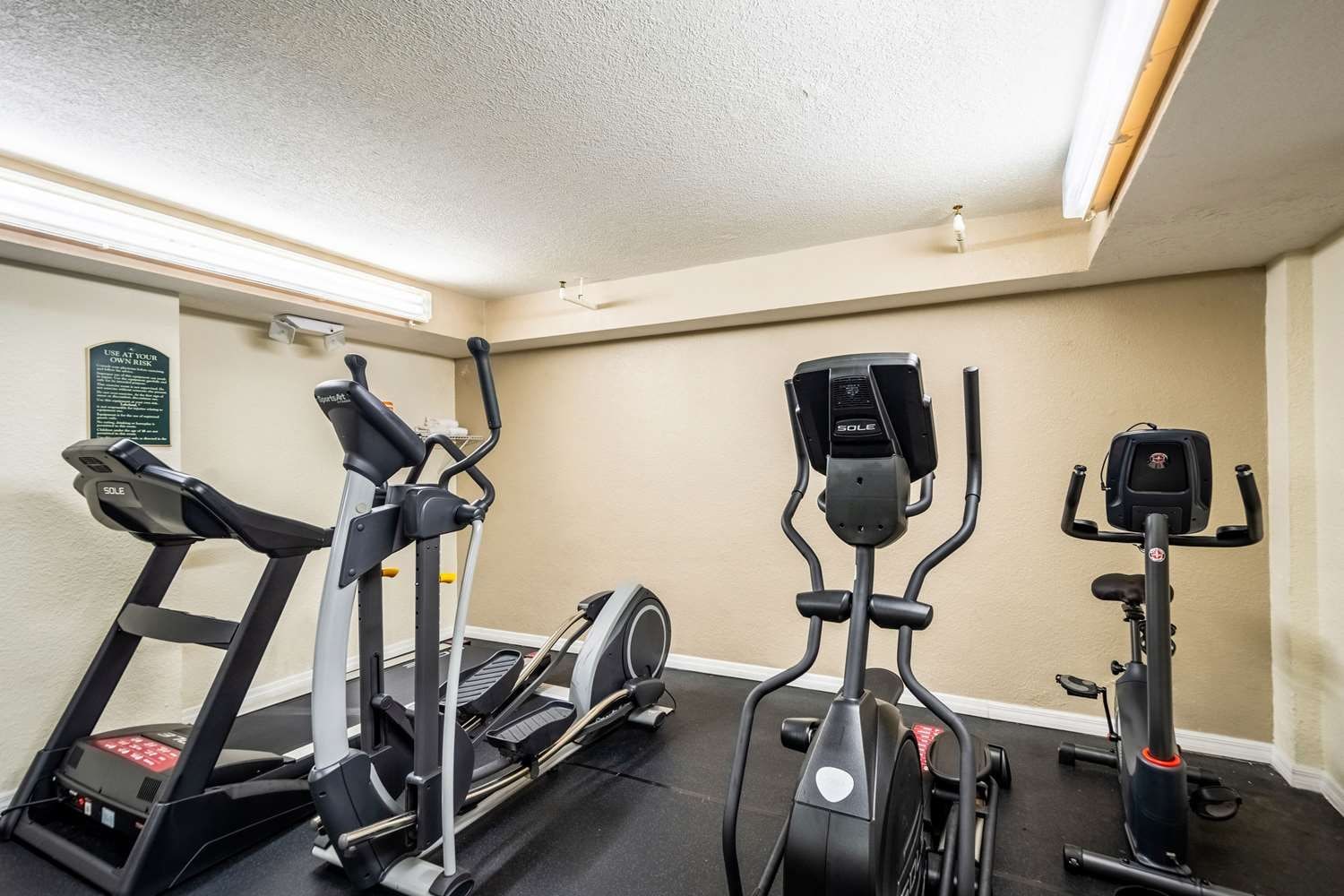 A fitness room with three stationary bikes, a treadmill, and a rowing machine.