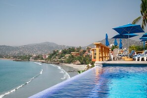Vista de la piscina con playa, sillas de descanso y sombrillas.