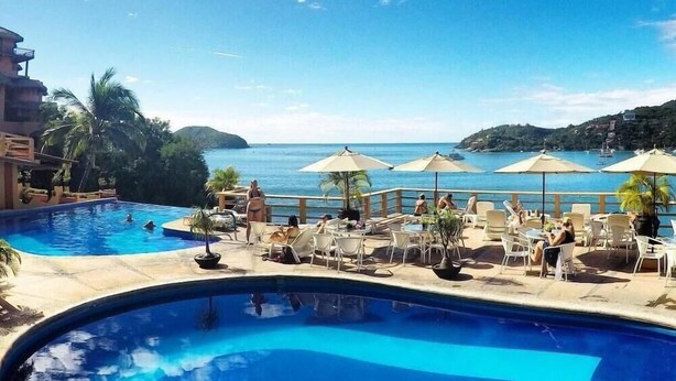 A pool area with lounge chairs and umbrellas, overlooking a body of water and hills.