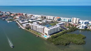 Vue aérienne d’un complexe hôtelier situé sur la côte, composé de plusieurs bâtiments, d’un port de plaisance et d’un vaste espace vert.