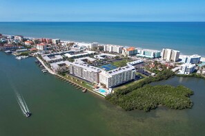 An aerial view of a coastal hotel complex with multiple buildings, a marina, and a large green area. - Waterfront Amenities, Walkable Dining & Gulf Beaches Nearby (Indian Shores)