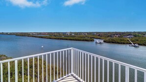 Une vue sur la rivière depuis un balcon doté d’une balustrade, un quai avec un bateau, et une côte lointaine parsemée de bâtiments.
