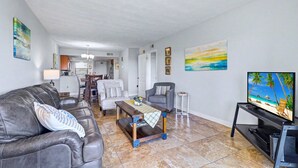 Un salon avec un canapé en cuir, une table basse en bois, un téléviseur posé sur un meuble et, au fond, un coin repas.