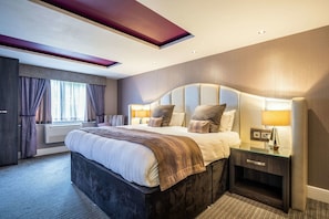 Ein modernes Hotelzimmer mit einem großen Bett, Nachttischlampen, einem Beistelltisch und einem Fenster mit Vorhängen.