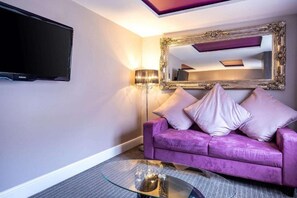 A room with a purple sofa, a flat-screen TV, a large mirror, and a floor lamp. - Clarion Hotel Newcastle South Boldon EN (Boldon Colliery)