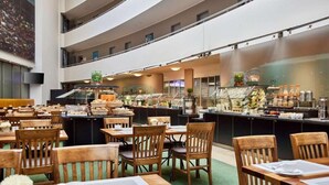 A multi-level dining area with wooden tables and chairs, a buffet counter, and a kitchen in the background. - Lindner Hotel Leverkusen Bayarena, Part of Jdv by Hyatt (Leverkusen)