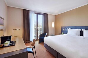 Ein Hotelzimmer mit Bett, Schreibtisch, Stuhl und Blick ins Freie durch ein Fenster.