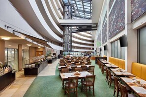 A spacious hotel dining area with multiple levels, a central buffet, and a high ceiling with skylights. - Lindner Hotel Leverkusen Bayarena, Part of Jdv by Hyatt (Leverkusen)