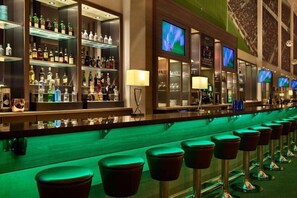 Un espace bar avec des étagères remplies de bouteilles d’alcool, des tabourets de bar et des téléviseurs.