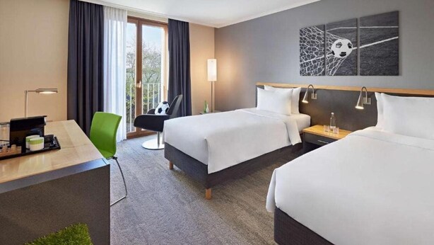 A hotel room with two beds, a desk, a chair, a desk lamp, and a wall art piece. - Lindner Hotel Leverkusen Bayarena, Part of Jdv by Hyatt (Leverkusen)