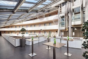A modern hotel lobby with a high ceiling, glass panels, and multiple dining areas. - Lindner Hotel Leverkusen Bayarena, Part of Jdv by Hyatt (Leverkusen)