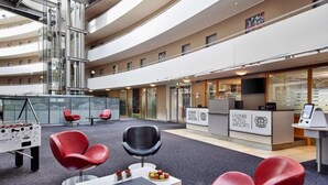 A modern hotel lobby with a high ceiling, multiple seating areas, a reception desk, and a visible staircase. - Lindner Hotel Leverkusen Bayarena, Part of Jdv by Hyatt (Leverkusen)