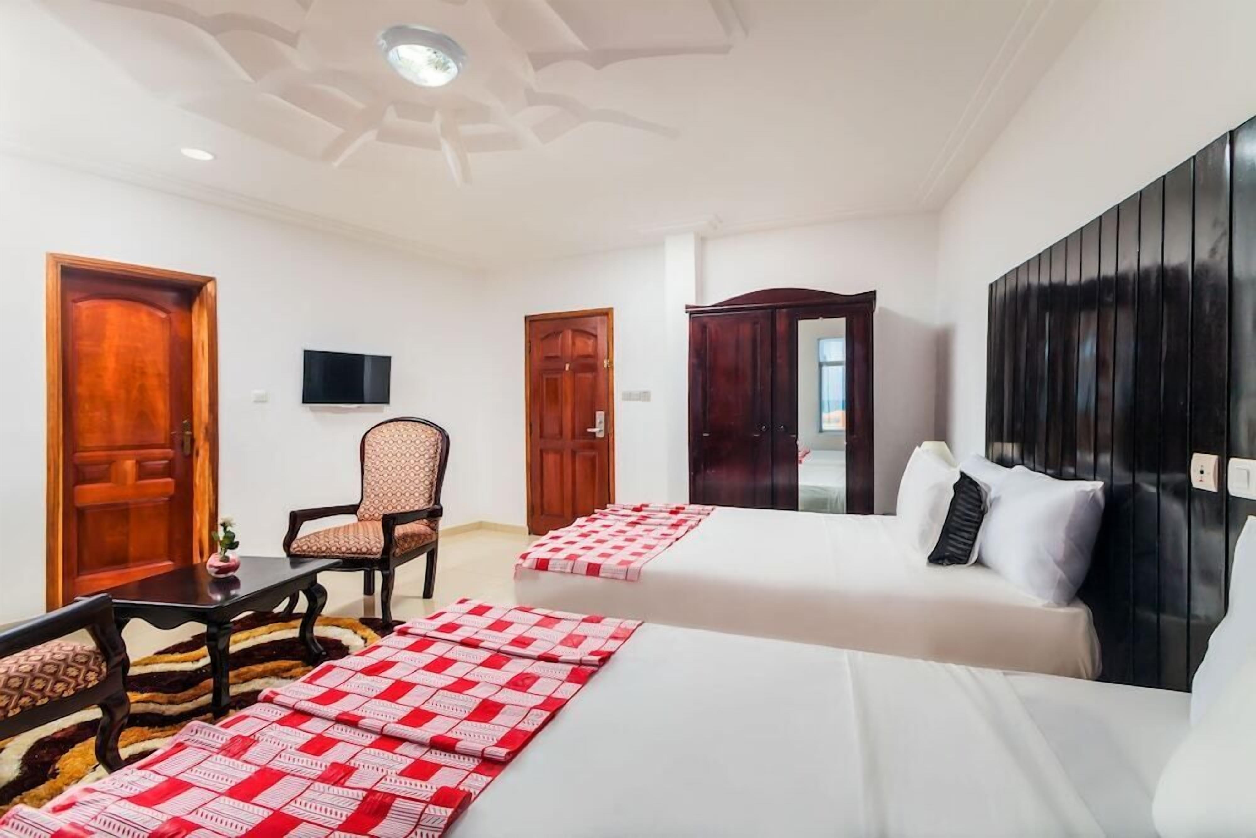 A hotel room with two beds, a television, a chair, and a desk.