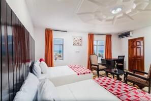 A hotel room with two beds, a desk, a chair, and a view of the city. - Hotel Bkbg (Lomé)