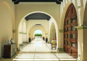 Un couloir orné d’arches, une grande porte en bois et un vase posé sur un piédestal.