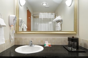 A hotel bathroom with a sink, mirror, towel rack, and shower curtain. - Olds Hotel (Olds)