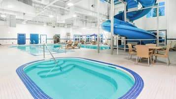 An indoor swimming pool with a blue slide, lounge chairs, and a table.