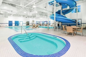 Una piscina interior con un tobogán azul, sillones de descanso y una mesa.